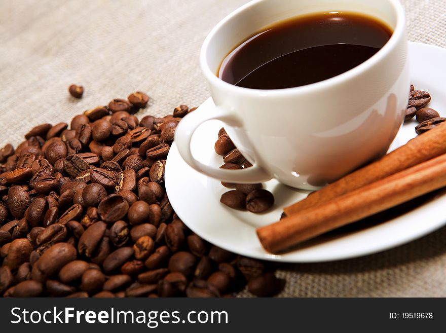 Cup of coffee with cinnamon tubes and grains of coffee. Cup of coffee with cinnamon tubes and grains of coffee