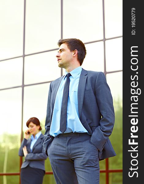 Businessman posing in front of business building and businesswoman in the background talking on the phone. Businessman posing in front of business building and businesswoman in the background talking on the phone