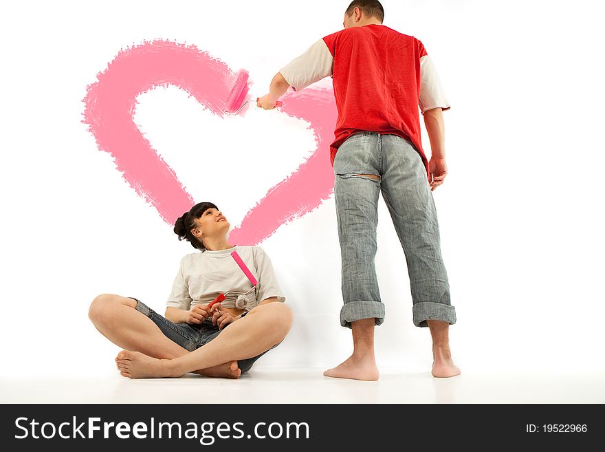 Young couple of workers painting heart on a wall with roller. Young couple of workers painting heart on a wall with roller