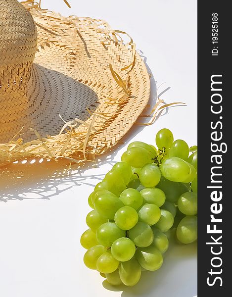 Straw hat and bunch of grapes on a white background