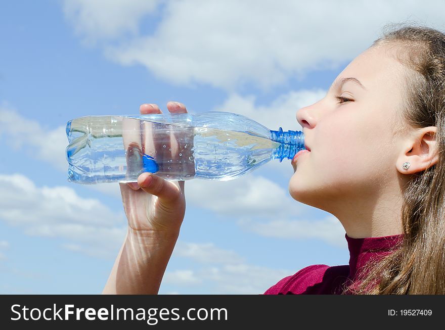 The girl drinks water against the sky