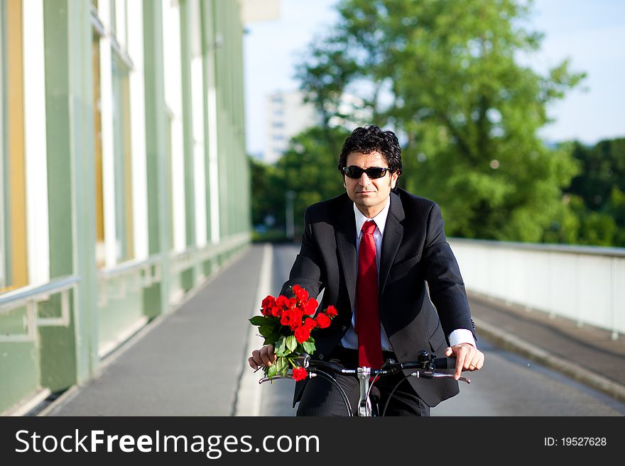 Businessman with suit is coming from work riding a bicycle with bouquet of red roses
