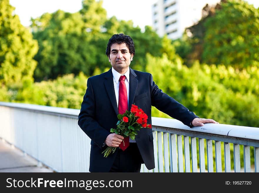 Businessman in a suit with bouquet of red roses standing on the bridge. Businessman in a suit with bouquet of red roses standing on the bridge