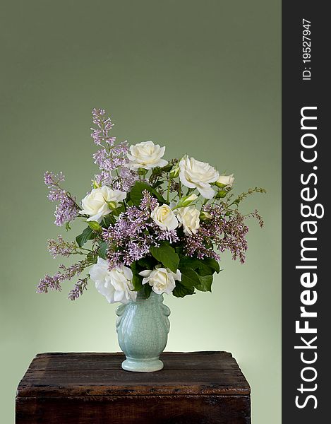 A spring flower arrangement with white roses and lilac in a antique vase with green background