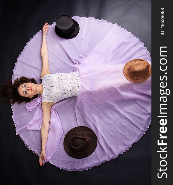 Attractive woman lying on the floor in liliac dress with a three hats