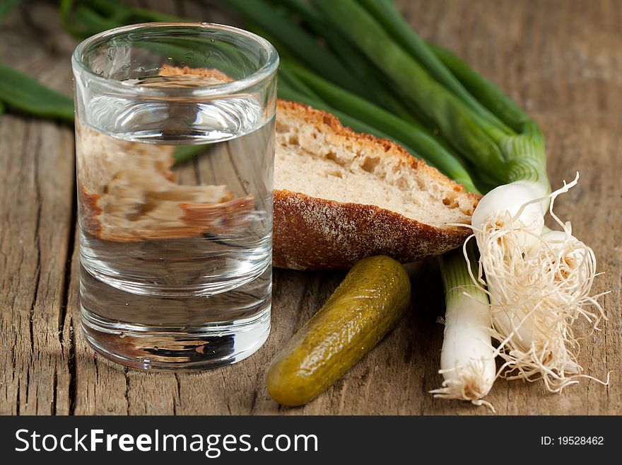 Glass of vodka with cucumber, onion and bread on old wooden table. Glass of vodka with cucumber, onion and bread on old wooden table
