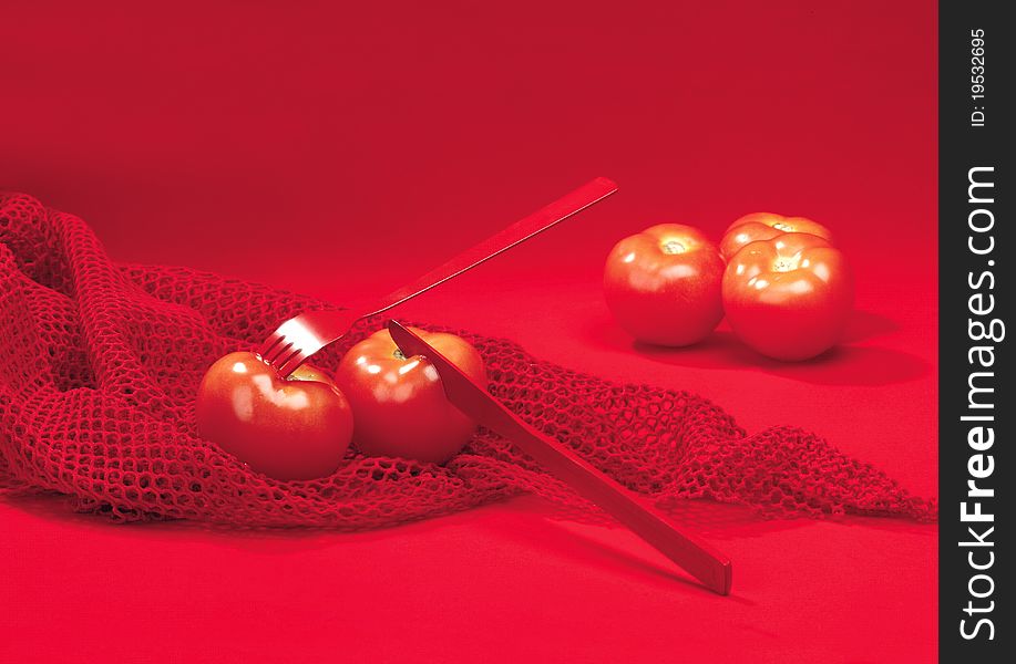 Two tomatoes cutting composition on a red fabric over a red background. Two tomatoes cutting composition on a red fabric over a red background
