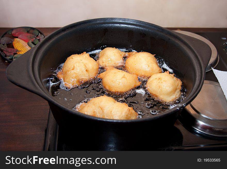 Frying balls of doughnut batter in hot oil in cast iron pot on a stove. Frying balls of doughnut batter in hot oil in cast iron pot on a stove