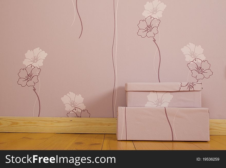 Purple wallpaper with flowers and a wooden floor in the room. On the floor there are two purple boxes. Purple wallpaper with flowers and a wooden floor in the room. On the floor there are two purple boxes