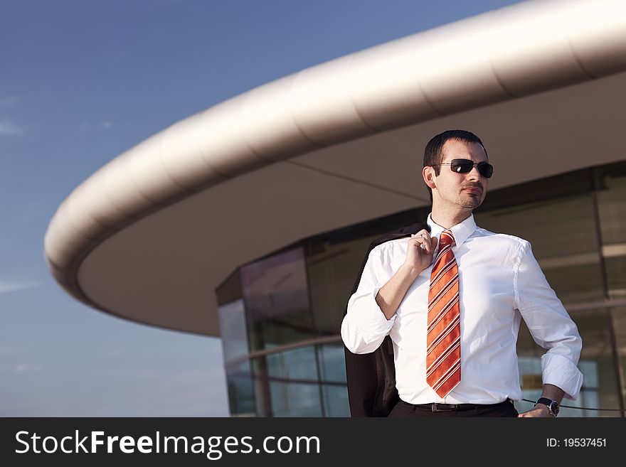 Serious young business person in white shirt, orange tie and sunglasses standing in front of office building with blue sky in background. Serious young business person in white shirt, orange tie and sunglasses standing in front of office building with blue sky in background.