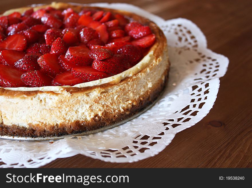 Detail of a whole home-made strawberry cheesecake on the decorative paper base located on a rustic wooden table.