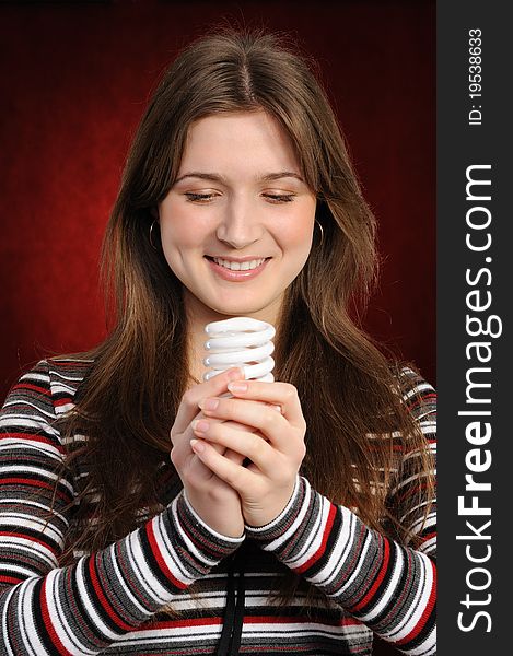 Young woman holding an fluorescent light bulb. On a red background