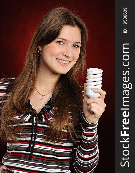 Young woman holding an fluorescent light bulb. On a red background