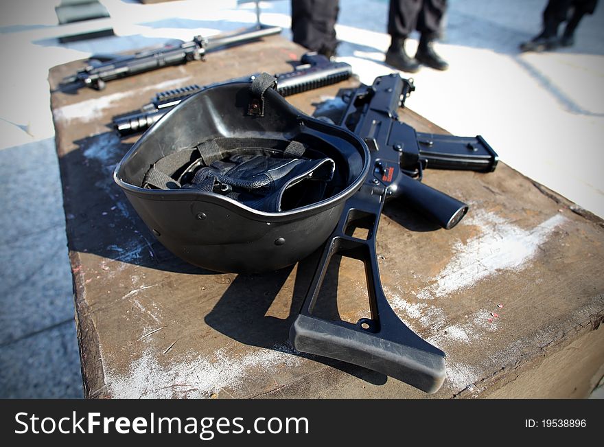 Helmet and a gun with police in the background.