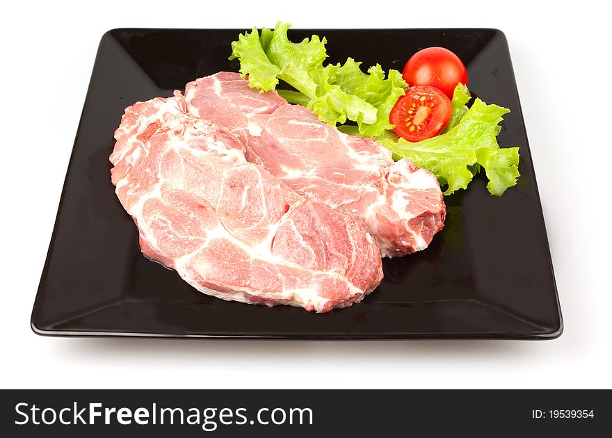 Pork steak with raw vegetables and greens on a black plate. Pork steak with raw vegetables and greens on a black plate