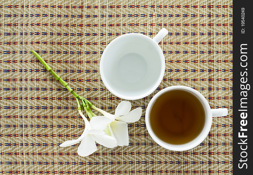 Cup of tea on a weaved mat with plumeria flower. Cup of tea on a weaved mat with plumeria flower