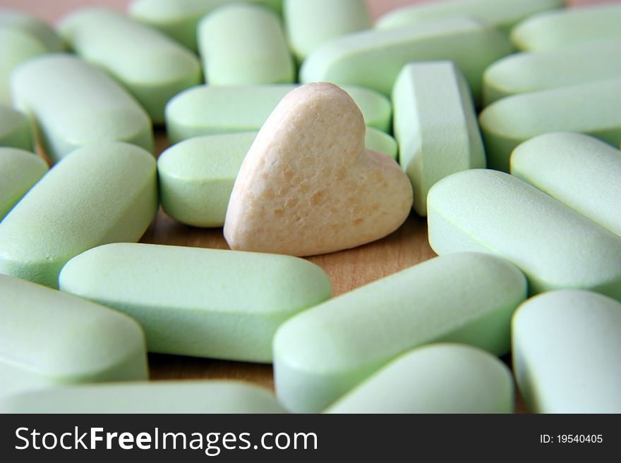 Grey tablet in the form of heart among green tablets