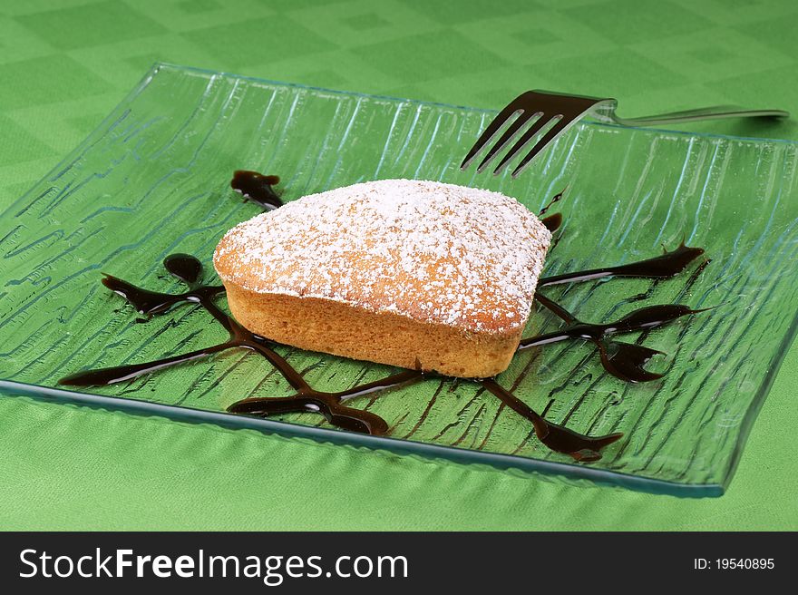 A small heart-shaped cake served on a glass palte over green tablecloth. Selective focus, shallow DOF