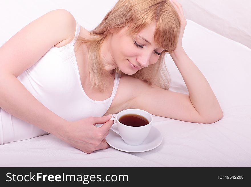 Young woman in bed holding a cup of tea after she waken up. Young woman in bed holding a cup of tea after she waken up