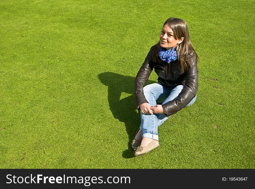 Attractive girl sitting on a green lawn. Spring.