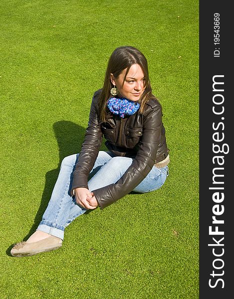 Attractive girl sitting on a green lawn. Spring.