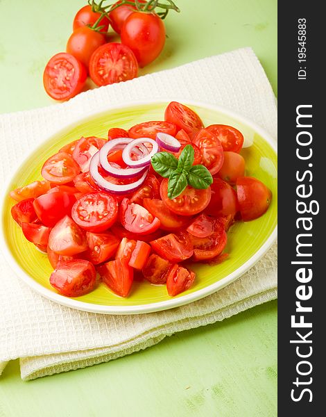 Fresh cutted cherry tomatoes with onion and basil on green plate. Fresh cutted cherry tomatoes with onion and basil on green plate