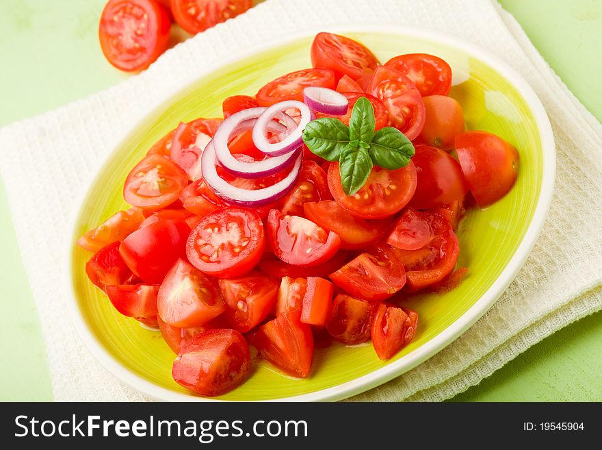 Fresh cutted cherry tomatoes with onion and basil on green plate. Fresh cutted cherry tomatoes with onion and basil on green plate