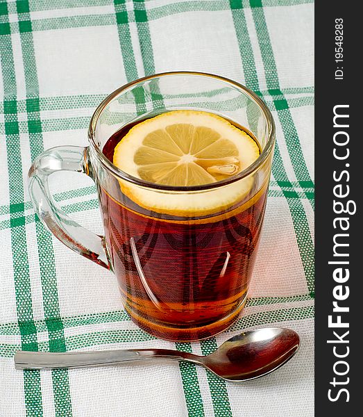 The cup of tea with a lemon stands on a checkered table-cloth