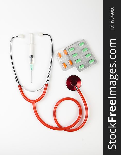 Single red shiny stethoscope with green and orange pills and a serynge on white background. Single red shiny stethoscope with green and orange pills and a serynge on white background