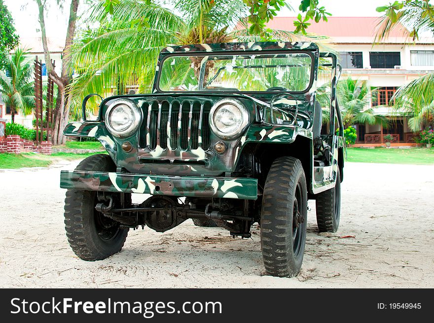 An all wheel drive camouflage painted jeep on a sandy ground and palm greenery background