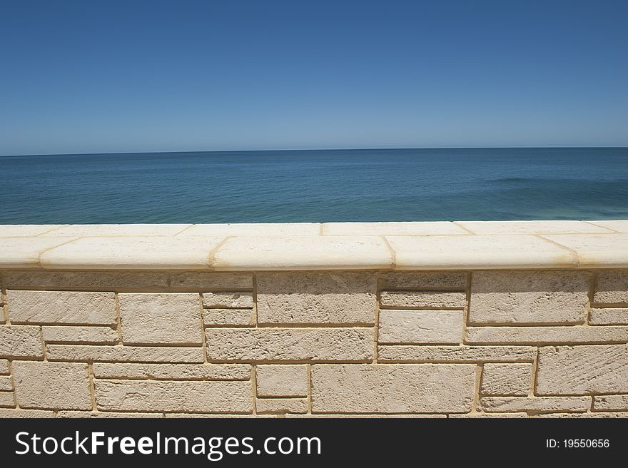 The vast open space of the sheer endless ocean and a clear blue sky behind a limestone wall.