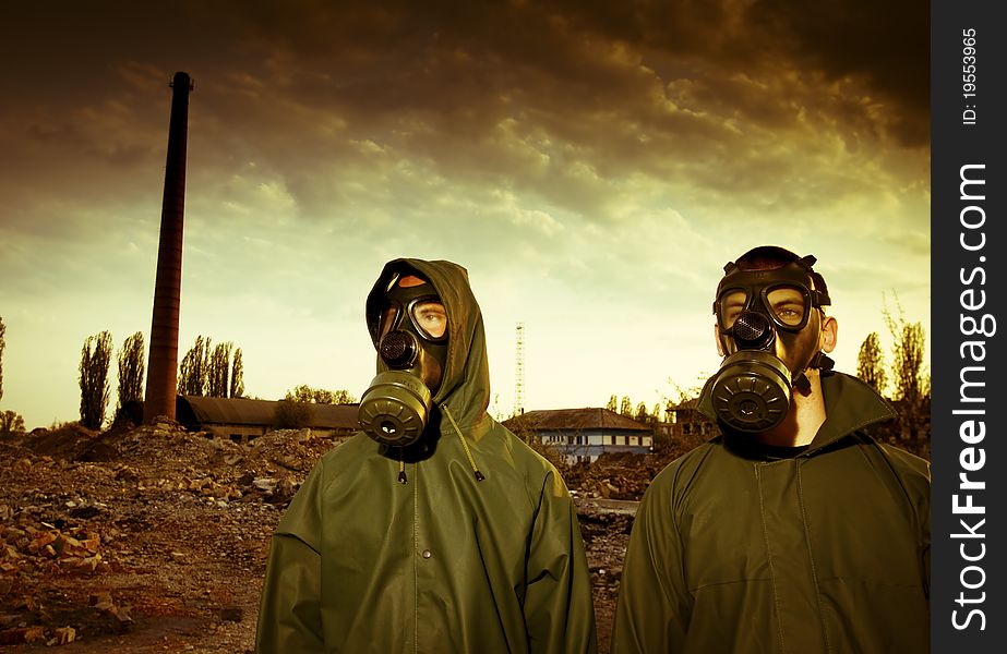 Two men in gas masks on smoky industrial background with pipes after nuclear disaster