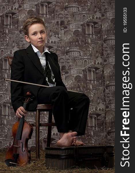 The tired boy in a classical suit sits on a chair with a violin in hands. The tired boy in a classical suit sits on a chair with a violin in hands