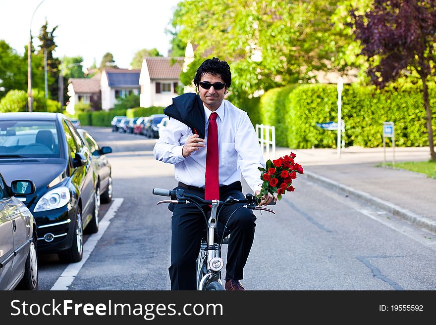 Businessman in a suit is riding a bicycle with bouquet of roses. Businessman in a suit is riding a bicycle with bouquet of roses