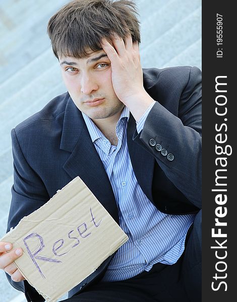 Young businessman sitting on the stairs of the building in hand bumga cardboard with the text reset with his other hand holding his head. Young businessman sitting on the stairs of the building in hand bumga cardboard with the text reset with his other hand holding his head