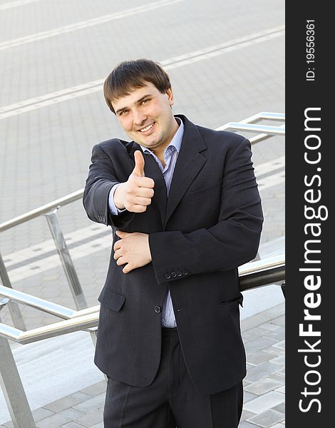 Young business man standing on the stairs of the building thumbs up. Young business man standing on the stairs of the building thumbs up