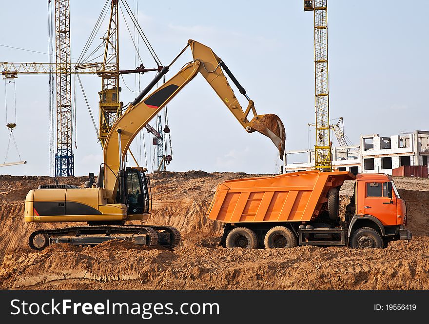 A backhoe loads the soil in a three-axle dump truck. A backhoe loads the soil in a three-axle dump truck