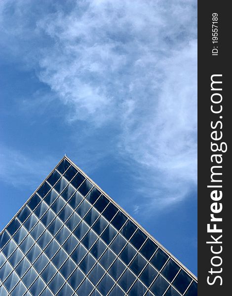 Top of glass pyramid-shaped building against blue sky and clouds. Top of glass pyramid-shaped building against blue sky and clouds.