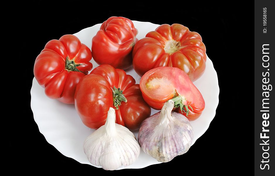 Fresh tomatoes and garlic on plate isolated over black