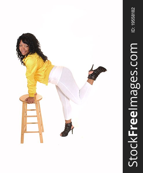 A young pretty African American woman standing in white tights and a yellow jacket, hands on a chair, for white background. A young pretty African American woman standing in white tights and a yellow jacket, hands on a chair, for white background.