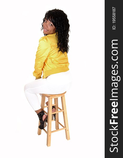 A young pretty African American woman sitting on an chair in white tights and a yellow jacket from the back, looking over her shoulder, for white background. A young pretty African American woman sitting on an chair in white tights and a yellow jacket from the back, looking over her shoulder, for white background.