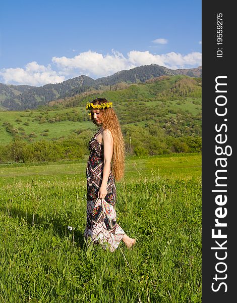 Girl wreaths on long hair is walking through the grass in the mountains. Girl wreaths on long hair is walking through the grass in the mountains