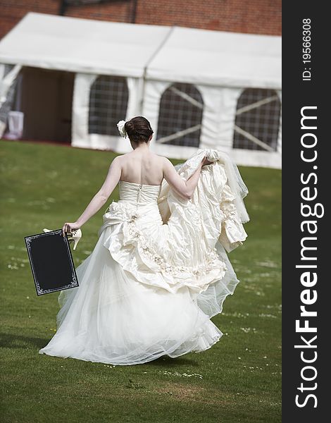 Pretty bride in wedding dress walking away from camera holding a blank board with space for copy. Pretty bride in wedding dress walking away from camera holding a blank board with space for copy