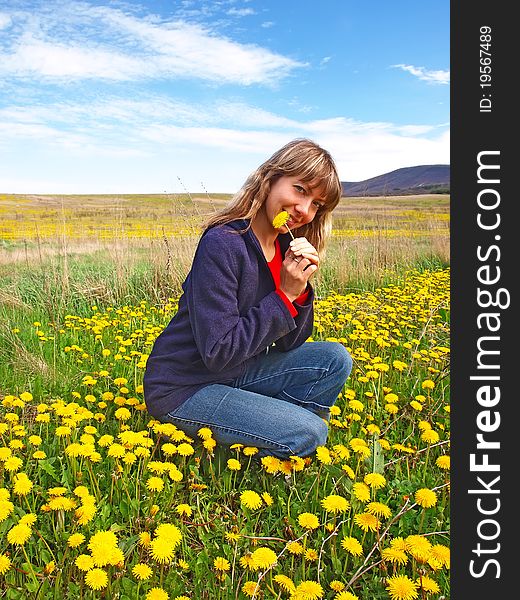 Smiling beautiful girl sitting on a dandelions field with dandelion in her hand. Smiling beautiful girl sitting on a dandelions field with dandelion in her hand