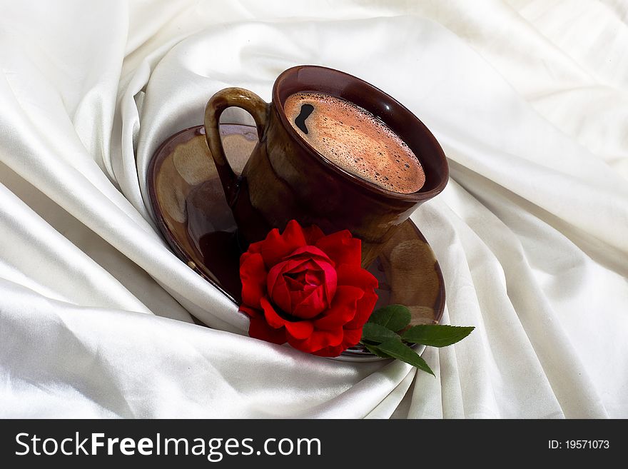 Cup of coffee with red rose on white fabric. Cup of coffee with red rose on white fabric