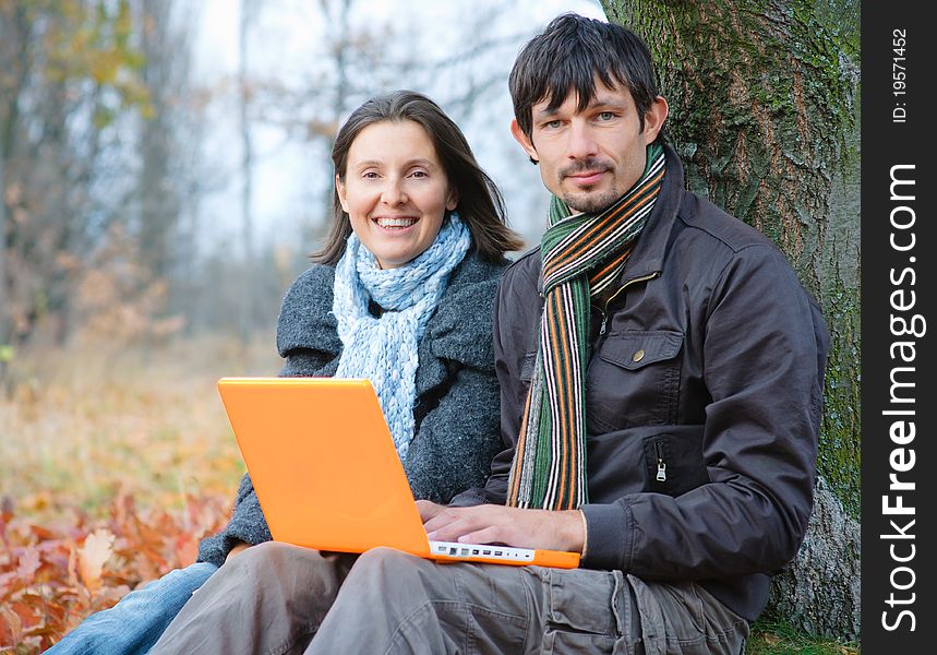 Romantic mature couple sitting with laptop in the autumn park. Romantic mature couple sitting with laptop in the autumn park.