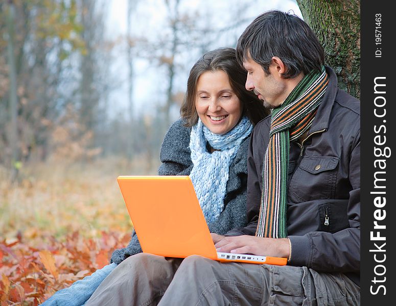 Romantic mature couple sitting with laptop in the autumn park. Romantic mature couple sitting with laptop in the autumn park.