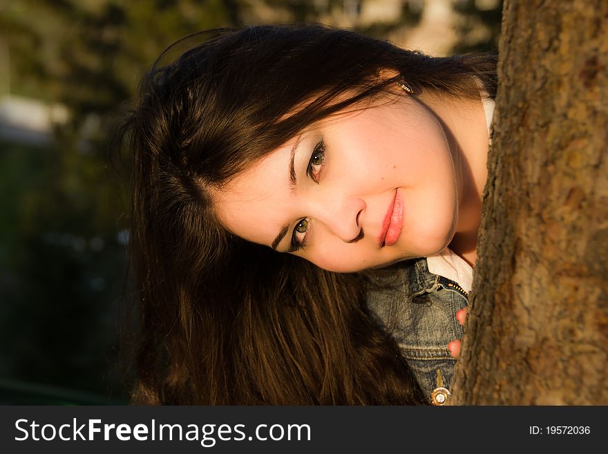 A long-haired brunette girl looking out the tree stem. A long-haired brunette girl looking out the tree stem