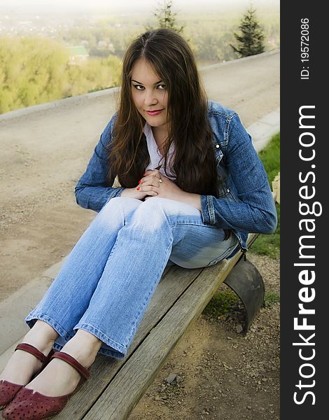 A long-haired brunette girl on a park bench plotting something. A long-haired brunette girl on a park bench plotting something