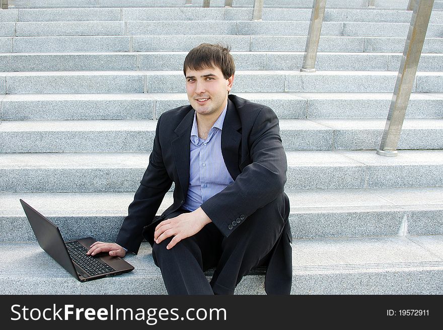 Modern business man outdoors sitting on the stairs of the building with a laptop